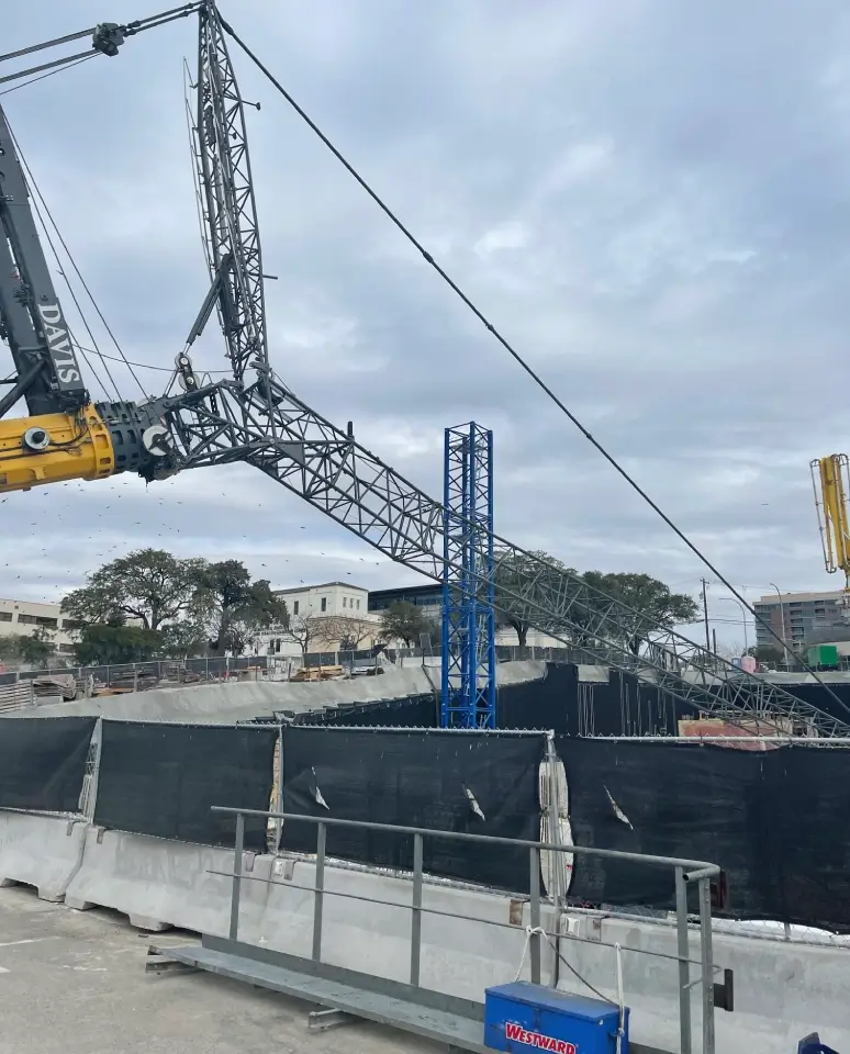 Construction site with cranes and black barriers under a cloudy sky.