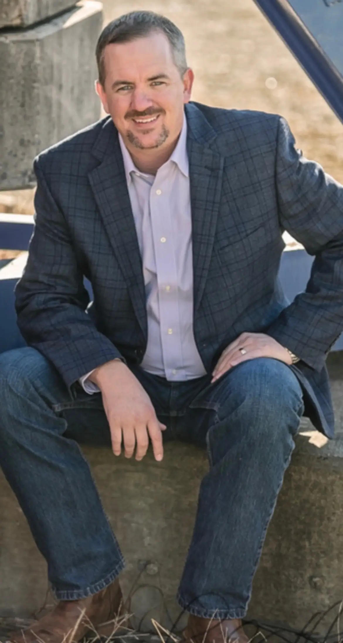 Man sitting casually wearing a blazer and jeans.