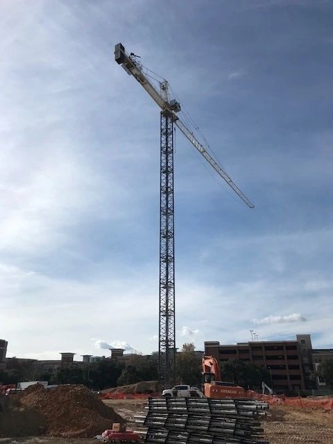 A tall construction crane towering over buildings under a partly cloudy sky.