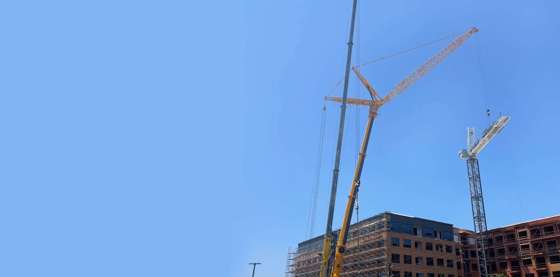 Crane lifting materials at a construction site against clear blue sky.