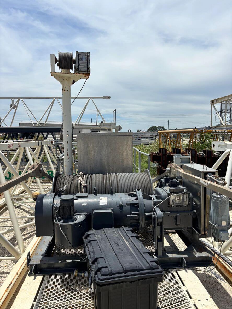 Industrial winch system with cable spool on a metal platform under a cloudy sky.