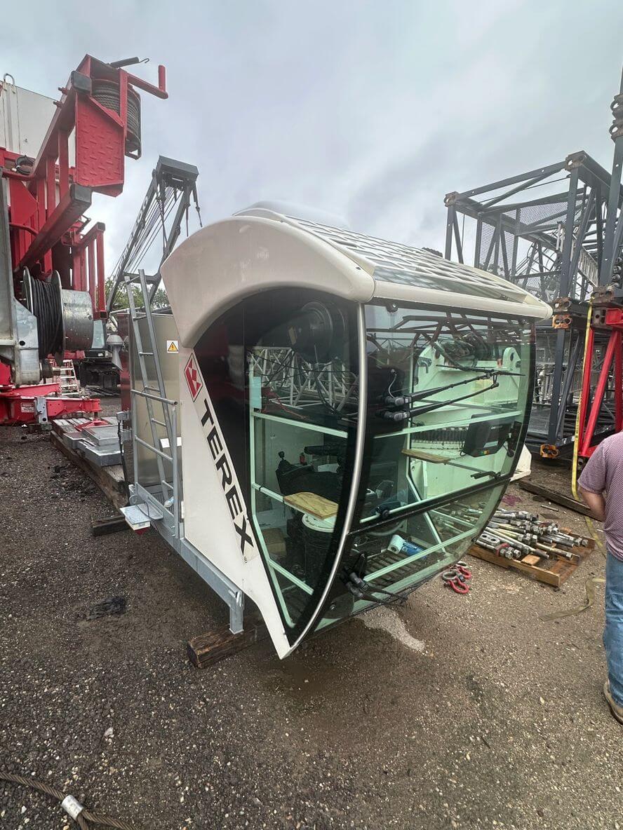 Overturned crane cabin resting on the ground at a construction site.